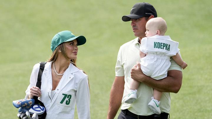 Apr 10, 2024; Augusta, Georgia, USA; Brooks Koepka carries his son, Crew, while walking near the no. 4 green with his wife, Jena Sims, during the Par 3 Contest at Augusta National Golf Club. Mandatory Credit: Michael Madrid-USA TODAY Network