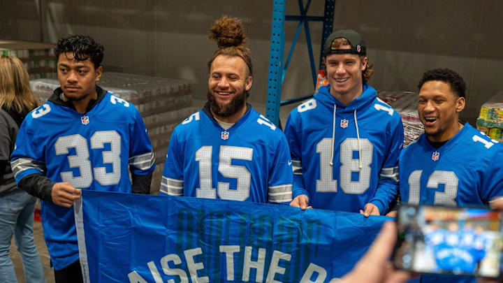 Detroit Lions players pose for a photo while holding a “Raise the Roar” banner during Community food bank event