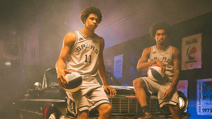San Antonio Spurs forward Carter Bryant (11) and guard Dylan Harper (2) pose for a photo while modeling the team's new ABA-style Nike Classic Edition uniforms. San Antonio Spurs forward Carter Bryant (11) and guard Dylan Harper (2) pose for a photo while modeling the team's new ABA-style Nike Classic Edition uniforms.