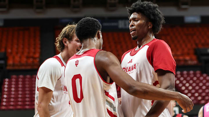 Indiana basketball forward Sam Alexis (right) chest bumps guard Jasai Miles (middle) while forward Reed Bailey (left) smiles.