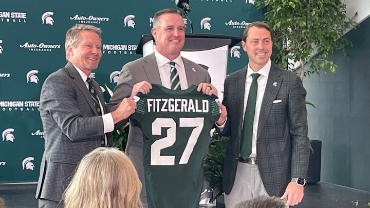 Michigan State Spartans head coach Pat Fitzgerald, center, poses with a namesake jersey next to MSU president Kevin Guskiewicz, left, and athletic director J Batt, right, during Fitzgerald's introductory press conference on Tuesday, Dec. 2, 2025.