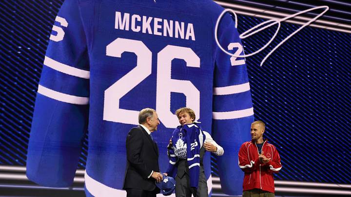 Jun 26, 2026; Buffalo, New York, USA; Gavin McKenna puts on a sweater beside NHL commissioner Gary Bettman and singer Justin Bieber after being selected with the first pick in the first round of the 2026 NHL Draft by the Toronto Maple Leafs at KeyBank Center. 