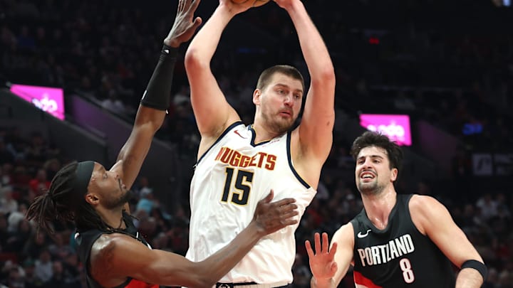 Feb 20, 2026; Portland, Oregon, USA;  Denver Nuggets center Nikola Jokic (15) grabs a rebound over Portland Trail Blazers guard Jrue Holiday (5) and forward Deni Avdija (8) during first half at Moda Center.
