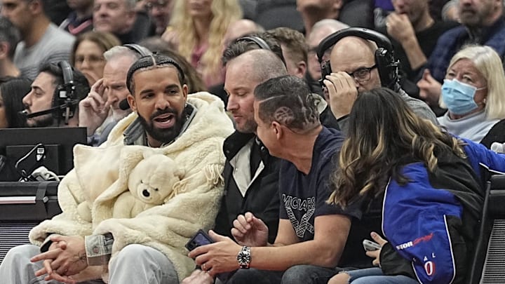 Nov 23, 2022; Toronto, Ontario, CAN; Recording artist Drake (white coat) sits courtside during a game between the Brooklyn Nets and Toronto Raptors at Scotiabank Arena. Mandatory Credit: John E. Sokolowski-Imagn Images