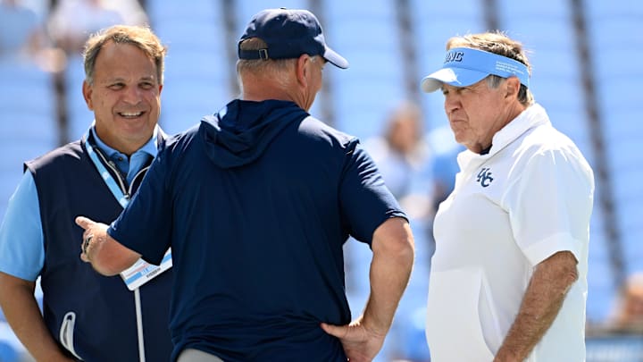 Sep 13, 2025; Chapel Hill, North Carolina, USA; Richmond Spiders head coach Russ Huesman talks to North Carolina Tar Heels general manger Michael Lombardi and head coach Bill Belichick before the game at Kenan Stadium. Mandatory Credit: Bob Donnan-Imagn Images