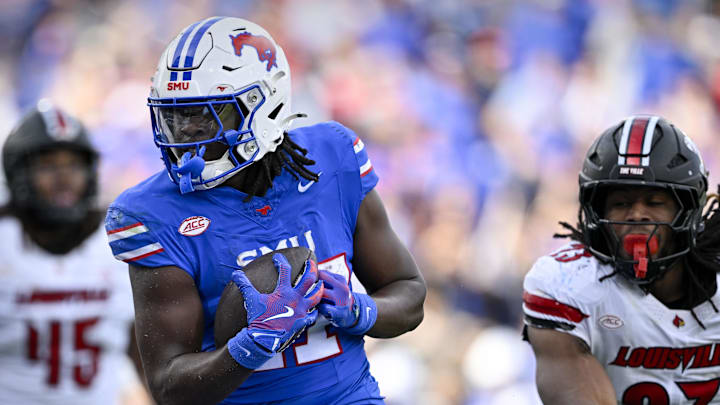 Nov 22, 2025; Dallas, Texas, USA; SMU Mustangs running back T.J. Harden (27) eludes the tackle of Louisville Cardinals defensive lineman Wesley Bailey (23) for a touchdown during the first half at Gerald J. Ford Stadium.