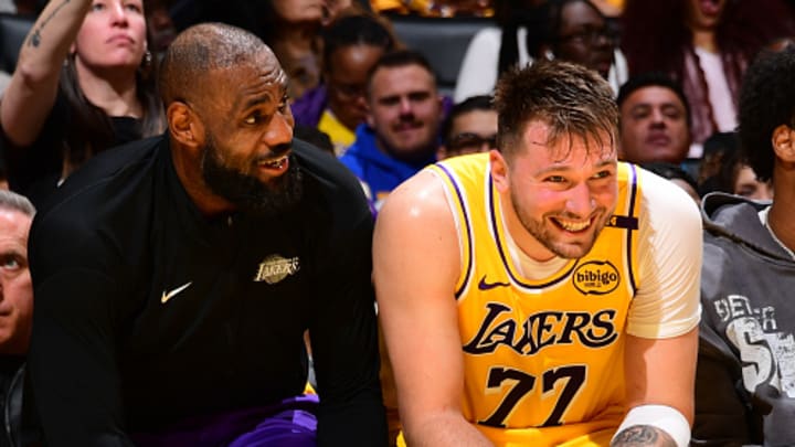 Los Angeles Lakers stars LeBron James and Luka Doncic laugh with each other on the bench.