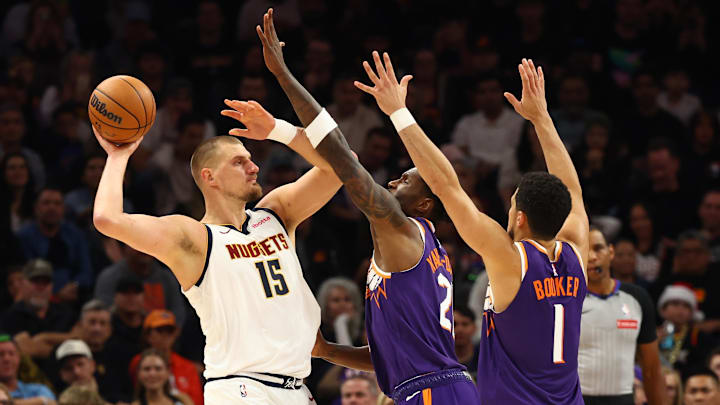 Nov 29, 2025; Phoenix, Arizona, USA; Denver Nuggets center Nikola Jokic (15) controls the ball against Phoenix Suns forward Nigel Hayes-Davis (21) and guard Devin Booker (1) in the first half at the Mortgage Matchup Center. Mandatory Credit: Mark J. Rebilas-Imagn Images