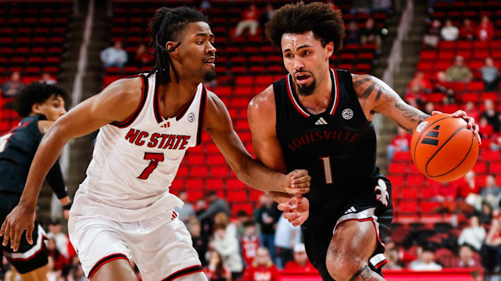 Feb 12, 2025; Raleigh, North Carolina, USA; Louisville Cardinals guard J'Vonne Hadley (1) dribbles with the ball guarded by North Carolina State Wolfpack guard Bryce Heard (7) during the second half of the game at Lenovo Center. Mandatory Credit: Jaylynn Nash-Imagn Images