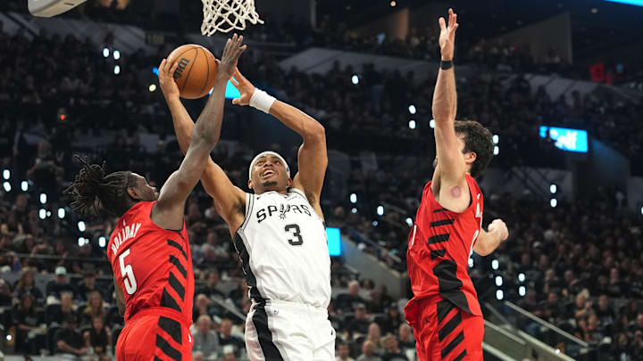 Apr 28, 2026; San Antonio, Texas, USA; San Antonio Spurs forward Keldon Johnson (3) drives to the basket against Portland Trail Blazers guard Jrue Holiday (5) and forward Deni Avdija (8) during the first half of Game 5 of the first round of the 2026 NBA Playoffs at Frost Bank Center.
