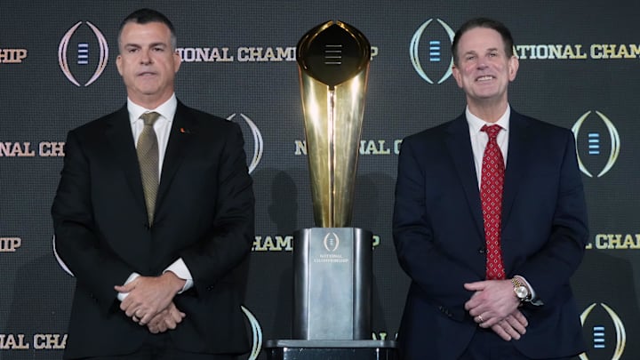 Jan 18, 2026; Miami, FL, USA; Miami Hurricanes coach Mario Cristobal (left) and Indiana Hoosiers coach Curt Cignetti pose with the national championship trophy during the CFP head coaches press conference at JW Marriott Marquis Miami.