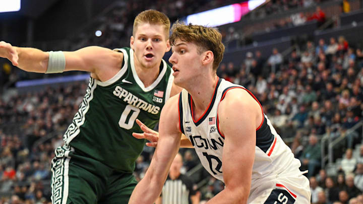 Oct 28, 2025; Hartford, CT, USA; Connecticut Huskies center Eric Reibe (12) controls the ball defended by Michigan State Spartans forward Jaxon Kohler (0) during the first half at PeoplesBank Arena. Mandatory Credit: Mark Smith-Imagn Images Oct 28, 2025; Hartford, CT, USA; Connecticut Huskies center Eric Reibe (12) controls the ball defended by Michigan State Spartans forward Jaxon Kohler (0) during the first half at PeoplesBank Arena. Mandatory Credit: Mark Smith-Imagn Images