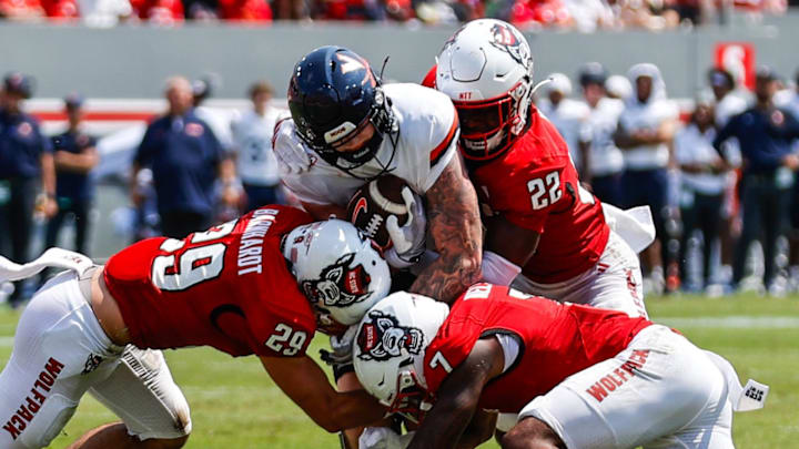 Sep 6, 2025; Raleigh, North Carolina, USA; Virginia Cavaliers tight end Sage Ennis (0) is tackled by North Carolina State Wolfpack safety Brody Barnhardt (29), cornerback Brian Nelson II (7) and cornerback Jackson Vick (22) during the first half of the game at Carter-Finley Stadium. Mandatory Credit: Jaylynn Nash-Imagn Images