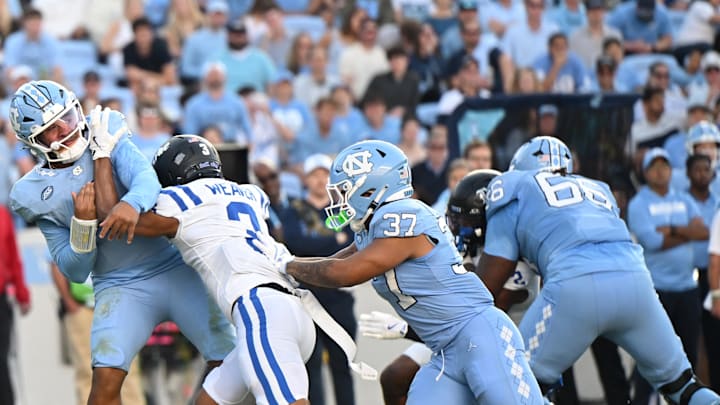Nov 22, 2025; Chapel Hill, North Carolina, USA; North Carolina Tar Heels quarterback Gio Lopez (7) is hit after a pass by Duke Blue Devils defensive back Caleb Weaver (3) during the first half at Kenan Stadium. Mandatory Credit: William Howard-Imagn Images