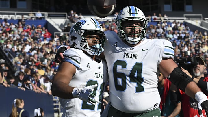 Nov 16, 2024; Annapolis, Maryland, USA; Tulane Green Wave running back Makhi Hughes (21) celebrates with offensive lineman Vincent Murphy (64) after scoring a touchdown against the Navy Midshipmen at Navy-Marine Corps Memorial Stadium. Mandatory Credit: Tommy Gilligan-Imagn Images Nov 16, 2024; Annapolis, Maryland, USA; Tulane Green Wave running back Makhi Hughes (21) celebrates with offensive lineman Vincent Murphy (64) after scoring a touchdown against the Navy Midshipmen at Navy-Marine Corps Memorial Stadium. Mandatory Credit: Tommy Gilligan-Imagn Images