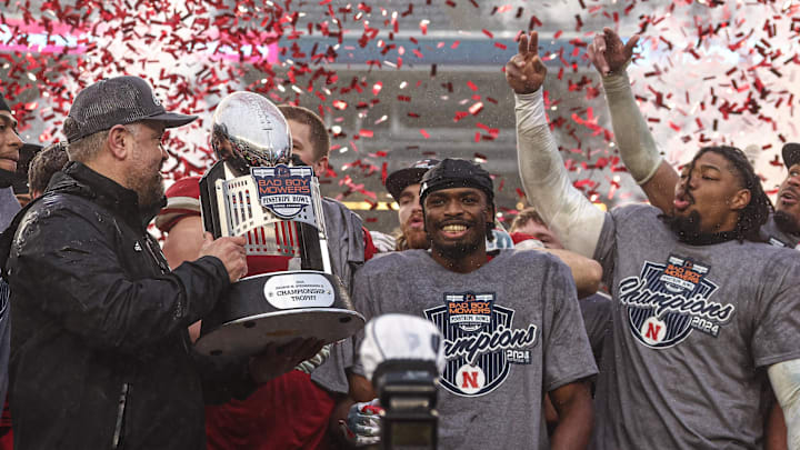 Head coach Matt Rhule holds the Pinstripe Bowl trophy as Nebraska players celebrate their win over Boston College.