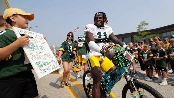 Green Bay Packers wide receiver Jayden Reed (11) laughs at a young fan's sign while riding to training camp.