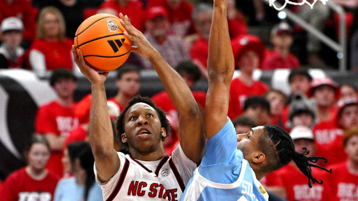 Feb 17, 2026; Raleigh, North Carolina, USA;  NC State Wolfpack guard Quadir Copeland (11) lays the ball up against North Carolina Tar Heels forward Jarin Stevenson (15) during the first half at Lenovo Center. Mandatory Credit: Zachary Taft-Imagn Images