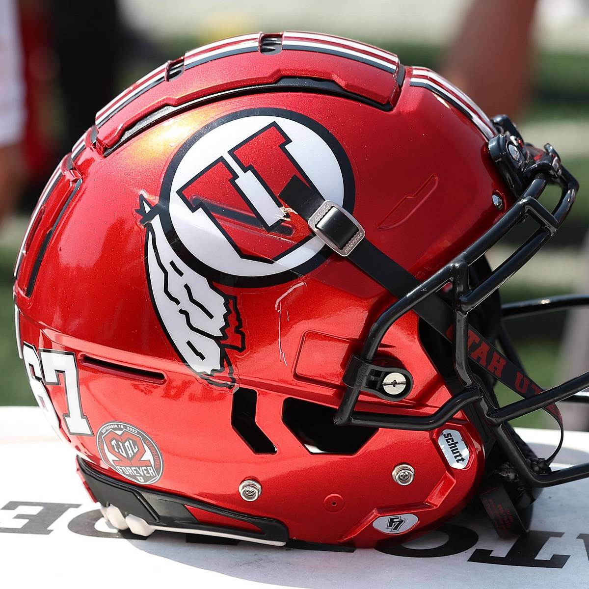Close-up documentary photograph of a red Utah Utes football helmet with the drum-and-feather emblem