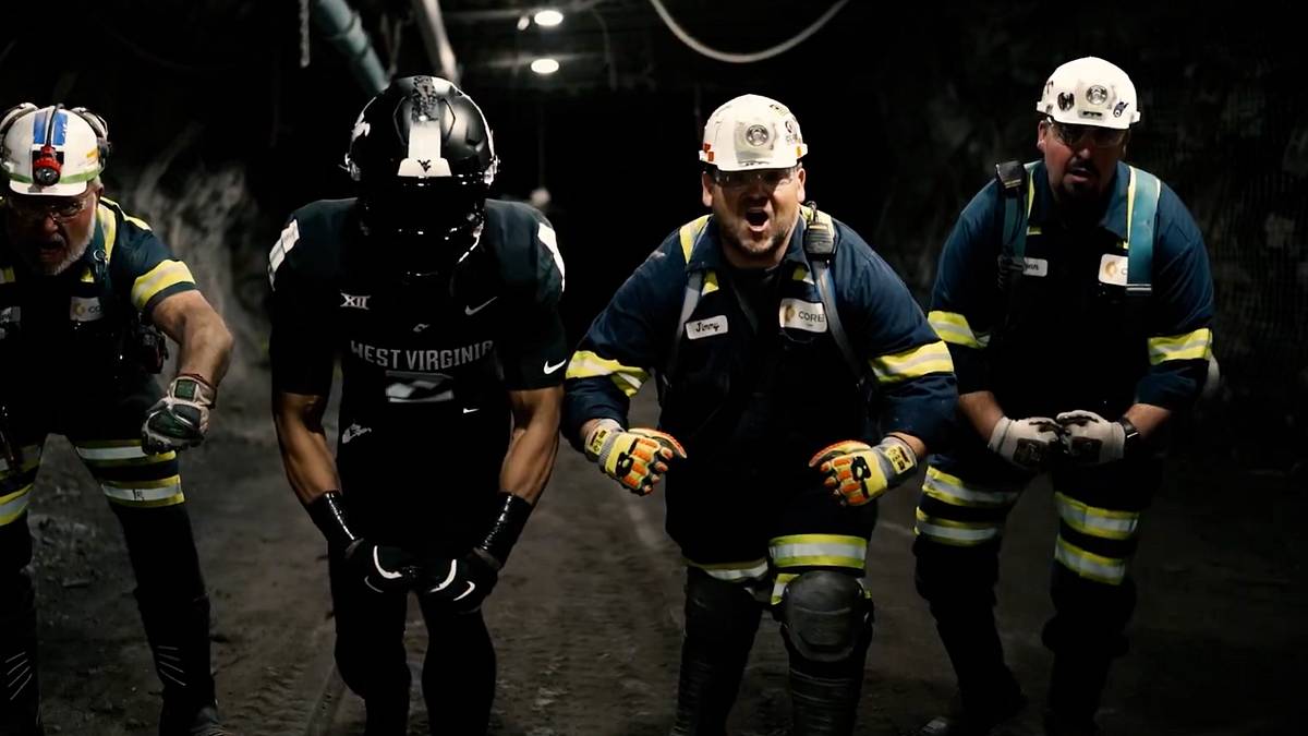 West Virginia Coal Rush uniform reveal with Mountaineer football player in black uniform standing alongside coal miners in underground protective gear