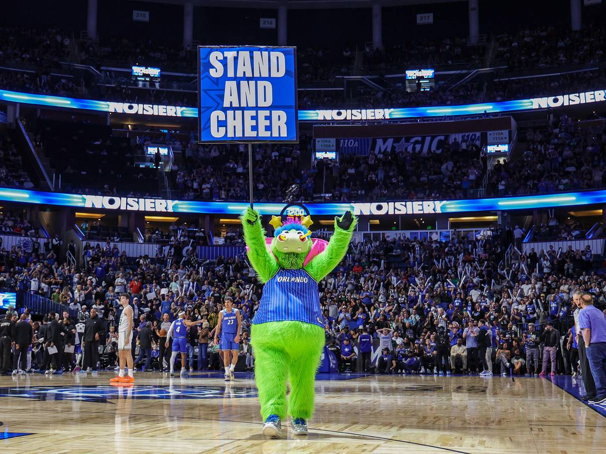 Orlando Magic mascot Stuff holding a Stand and Cheer sign on the Kia Center court