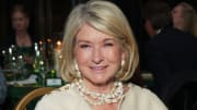 Martha Stewart wears a white coat and pearl necklaces and smiles for the camera.