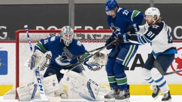 VANCOUVER, BC - MARCH 22: Goalie Thatcher Demko #35 of the Vancouver Canucks eyes the puck as Kyle Connor #81 of the Winnipeg Jets and Travis Hamonic #27 of the Vancouver Canucks battle in front of the net during the second period of NHL action at Rogers Arena on March 22, 2021 in Vancouver, Canada. (Photo by Rich Lam/Getty Images)