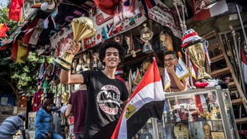 An Egyptian youth holds a replica model of the Afican Cup of Nations trophy in one hand an a national flag in the other as he stands outside a shop selling trophies and medals and other sports memorabilia in the capital Cairo's downtown district on June 17, 2019. (Photo by Khaled DESOUKI / AFP) (Photo credit should read KHALED DESOUKI/AFP/Getty Images)