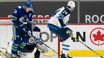 VANCOUVER, BC - MARCH 22: Bo Horvat #53 of the Vancouver Canucks reacts after getting hit with the puck while standing in front of goalie Connor Hellebuyck #37 of the Winnipeg Jets during the third period of NHL action at Rogers Arena on March 22, 2021 in Vancouver, Canada. (Photo by Rich Lam/Getty Images)