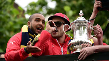 Arsenal's English midfielder Jack Wilshere (R) and Arsenal's English midfielder Theo Walcott hold the trophy as they stand on the top deck of an open-topped bus during the Arsenal victory parade in London on May 31, 2015, following their win in the English FA Cup final football match on May 30, 2014 against Aston Villa. Arsene Wenger's side made history at Wembley with a 4-0 rout of Aston Villa that underlined their renaissance in the second half of the campaign and served as a warning to English champions Chelsea. AFP PHOTO / LEON NEAL (Photo credit should read LEON NEAL/AFP/Getty Images)
