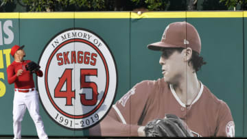 ANAHEIM, CA - SEPTEMBER 27: Hansel Robles #57 of the Los Angeles Angels looks at a ball as it goes over the wall and a photo of Tyler Skaggs #45 during batting practice before playing the Houston Astros at Angel Stadium of Anaheim on September 27, 2019 in Anaheim, California. (Photo by John McCoy/Getty Images)