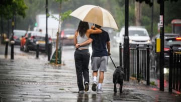 LONDON, ENGLAND - AUGUST 17: A couple shelter under an umbrella during a dog walk, as torrential rain and thunderstorms hit the country on August 17, 2022 in London, England. After the UK experienced a second summer heatwave, storms are expected starting in the north of the country from Monday moving to the whole country by Wednesday, with flood alerts issued by the Met Office. (Photo by Leon Neal/Getty Images)