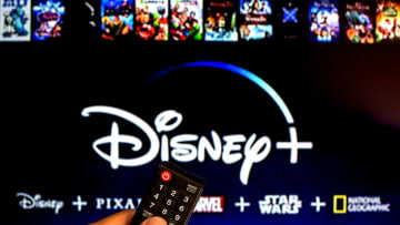 SPAIN - 2021/07/13: In this photo illustration a close-up of a hand holding a TV remote control seen displayed in front of the Disney+ logo. (Photo Illustration by Thiago Prudencio/SOPA Images/LightRocket via Getty Images)