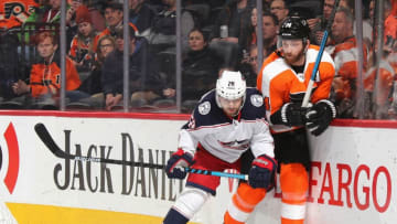 PHILADELPHIA, PENNSYLVANIA - FEBRUARY 18: Sean Couturier #14 of the Philadelphia Flyers is hit into the boards by Oliver Bjorkstrand #28 of the Columbus Blue Jackets during the second period at the Wells Fargo Center on February 18, 2020 in Philadelphia, Pennsylvania. (Photo by Bruce Bennett/Getty Images)