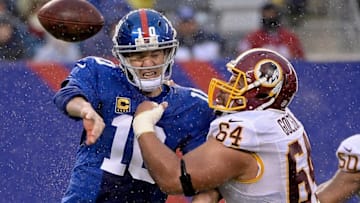 Dec 29, 2013; East Rutherford, NJ, USA; New York Giants quarterback Eli Manning (10) throws away a pass as he is hit by Washington Redskins defensive end Kedric Golston (64) in the first half during the game at MetLife Stadium. Mandatory Credit: Robert Deutsch-USA TODAY Sports