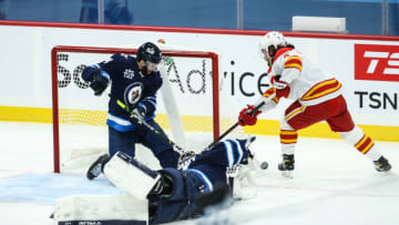 Jan 14, 2021; Winnipeg, Manitoba, CAN;Winnipeg Jets goalie Connor Hellebuyck (37) makes a save on Calgary Flames forward Rasmus Andersson (4) during the first period at Bell MTS Place. Mandatory Credit: Terrence Lee-USA TODAY Sports