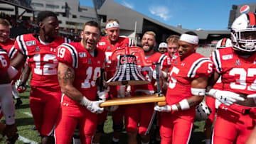 Members of the Cincinnati Bearcats carry the Victory Bell after win over Miami. The Enquirer.