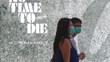 SINGAPORE - MARCH 29: Shoppers wearing protective masks walk past a James Bond upcoming movie 'No Time To Die' advertising billboard on March 29, 2020 in Singapore. The Ministry of Health has reported 70 new COVID-19 cases in a new high, bringing the country's total to 802. (Photo by Suhaimi Abdullah/Getty Images)