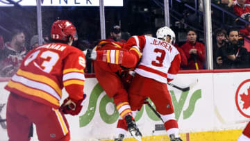 CALGARY, AB - JANUARY 18: Detroit Red Wings Defenceman Nick Jensen (3) checks Calgary Flames Defenceman T.J. Brodie (7) into the board during the second period of an NHL game where the Calgary Flames hosted the Detroit Red Wings on January 18, 2019, at the Scotiabank Saddledome in Calgary, AB. (Photo by Brett Holmes/Icon Sportswire via Getty Images)