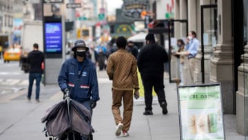 NEW YORK, NEW YORK - MARCH 24: A USPS mail woker wearing a mask walks past a "were open" sign on March 24, 2021 in New York City. After undergoing various shutdown orders for the past 12 months the city is currently in phase 4 of its reopening plan, allowing for the reopening of low-risk outdoor activities, movie and television productions, indoor dining as well as the opening of movie theaters, all with capacity restrictions. (Photo by Alexi Rosenfeld/Getty Images)