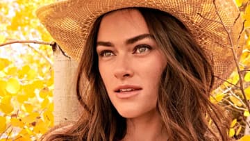 Myla Dalbesio poses in front of the bright yellow leaves in a tan straw cowgirl hat.