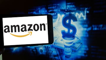 The logo of the American online shopping giant Amazon is seen on a screen next to an illustration of the stock market. Amazon is one of the biggest companies in the world. (Photo by Alexander Pohl/NurPhoto via Getty Images)