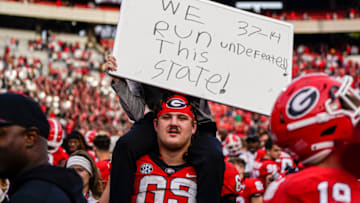 Nov 26, 2022; Athens, Georgia, USA; Georgia Bulldogs offensive lineman Tate Ratledge (69) and head coach Kirby Smart’s son Andrew react with a sign after defeating the Georgia Tech Yellow Jackets at Sanford Stadium. Mandatory Credit: Dale Zanine-USA TODAY Sports