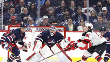 Winnipeg Jets right wing Nino Niederreiter (62) and New Jersey Devils center Dawson Mercer (91) reach for the puck in front of Winnipeg Jets goaltender Connor Hellebuyck (37) in the second period at Canada Life Centre. Mandatory Credit: James Carey Lauder-USA TODAY Sports