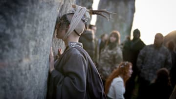 AMESBURY, ENGLAND - DECEMBER 22: A woman holds one of the stones as druids, pagans and revellers gather at Stonehenge, hoping to see the sun rise, as they take part in a winter solstice ceremony at the ancient neolithic monument of Stonehenge near Amesbury on December 22, 2018 in Wiltshire, England. A large crowd gathered at the famous historic stone circle, a UNESCO listed ancient monument to celebrate the sunrise closest to the Winter Solstice, the shortest day of the year. The event is claimed to be more important in the pagan calendar than the summer solstice, because it marks the 're-birth' of the Sun for the New Year. (Photo by Matt Cardy/Getty Images)