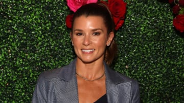 Danica Patrick poses in front of a green background in a gray plaid blazer and silver necklace.
