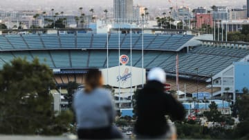 LOS ANGELES, CALIFORNIA - MARCH 26: People sit on a hill overlooking Dodger Stadium on what was supposed to be Major League Baseball's opening day, now postponed due to the coronavirus, on March 26, 2020 in Los Angeles, California. The Los Angeles Dodgers were slated to play against the San Francisco Giants at the stadium today. Major League Baseball Commissioner Rob Manfred recently said the league is "probably not gonna be able to" play a full 162 game regular season due to the spread of COVID-19. (Photo by Mario Tama/Getty Images)