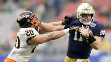 GLENDALE, ARIZONA - JANUARY 01: Jack Coan #17 of the Notre Dame Fighting Irish runs with the ball while being chased by Malcolm Rodriguez #20 of the Oklahoma State Cowboys in the second quarter during the PlayStation Fiesta Bowl at State Farm Stadium on January 01, 2022 in Glendale, Arizona. (Photo by Christian Petersen/Getty Images)