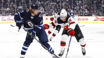 Dec 3, 2021; Winnipeg, Manitoba, CAN; Winnipeg Jets left wing Kyle Connor (81) shoots the puck past New Jersey Devils right wing Nathan Bastian (14) in the second period at Canada Life Centre. Mandatory Credit: James Carey Lauder-USA TODAY Sports