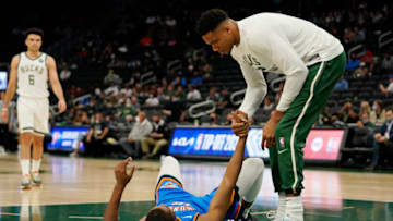 Giannis Antetokounmpo #34 of the Milwaukee Bucks helps Mamadi Diakite #12 of the Oklahoma City Thunder up off the court in the second half during a preseason game at Fiserv Forum on October 10, 2021 in Milwaukee, Wisconsin. NOTE TO USER: User expressly acknowledges and agrees that, by downloading and or using this photograph, user is consenting to the terms and conditions of the Getty Images License Agreement. (Photo by Patrick McDermott/Getty Images)